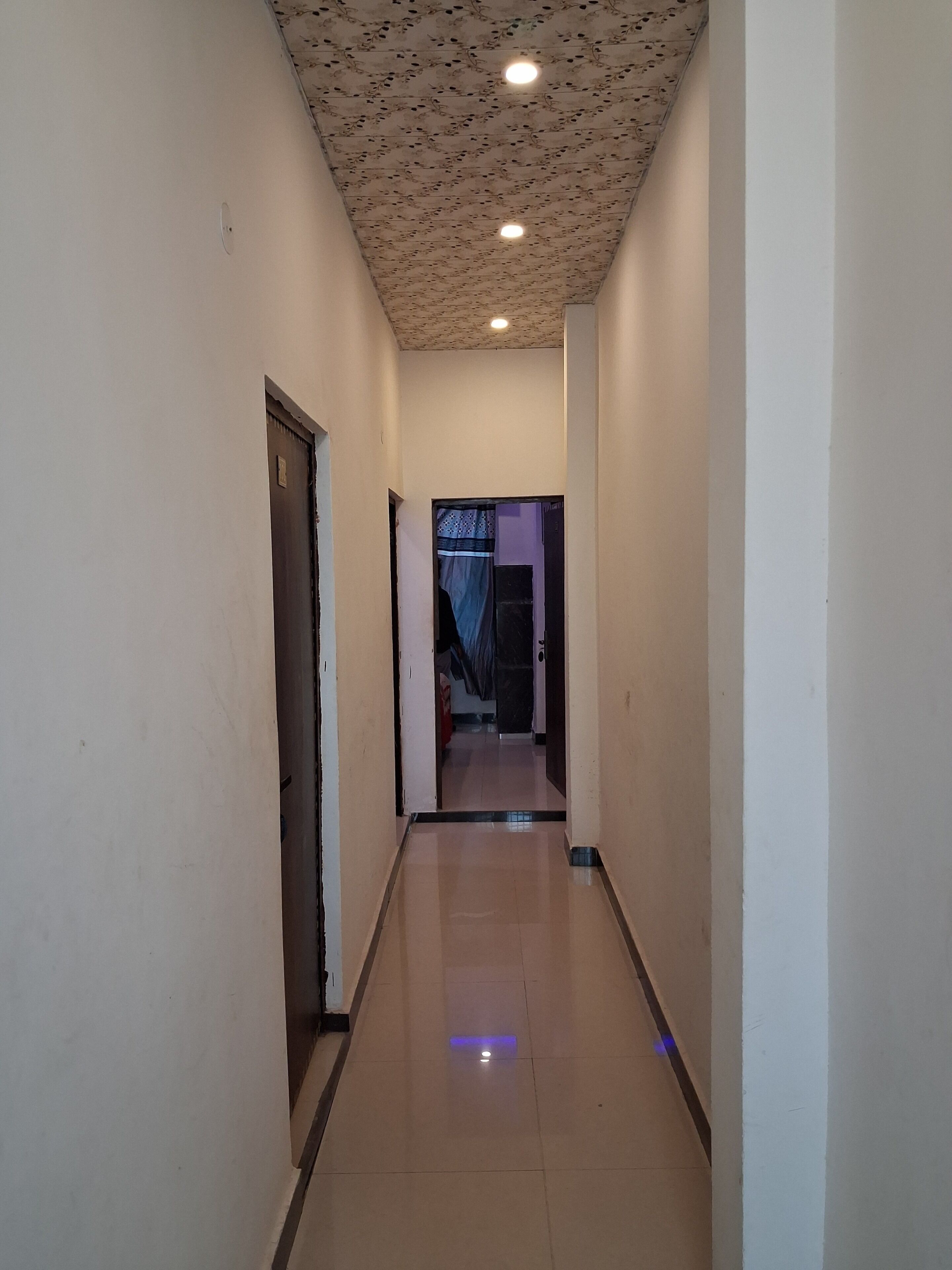 A corridor with a tiled floor, a door on the left, and a light fixture on the ceiling.