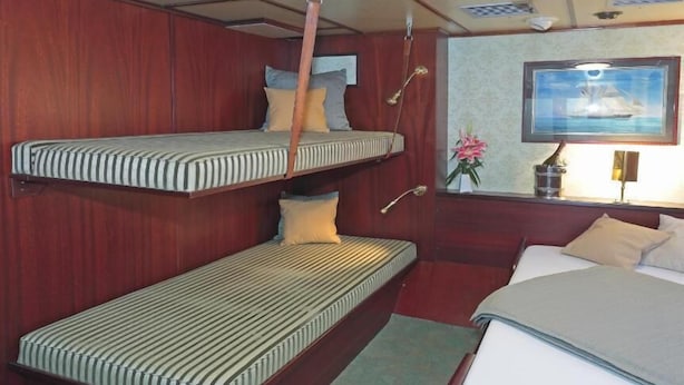 A cabin with bunk beds, a single bed, a small table, and a wall-mounted TV. - Sanssouci Star - Exclusive Island Cruise (Flensburg)