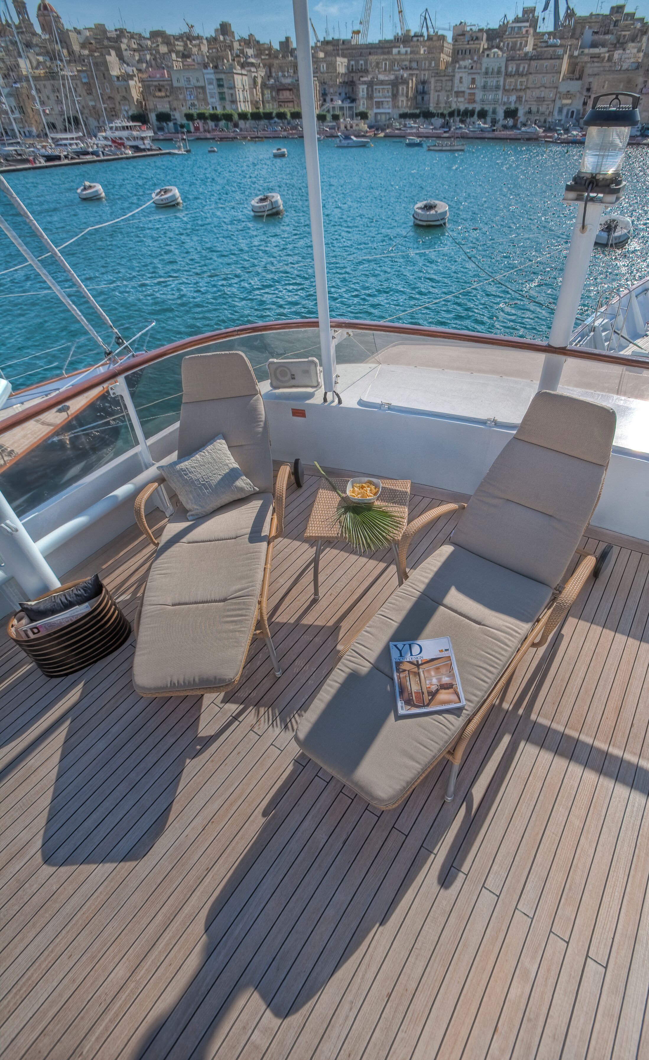 Une terrasse dotée de chaises longues et d’une table, offrant une vue sur un port de plaisance rempli de bateaux.