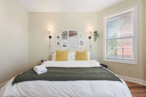 A bedroom with a bed, pillows, a blanket, wall art, a window with blinds, and a plant. - 9BR Family Retreat w/ BBQ & Parking Near Shopping (Pittsburgh)