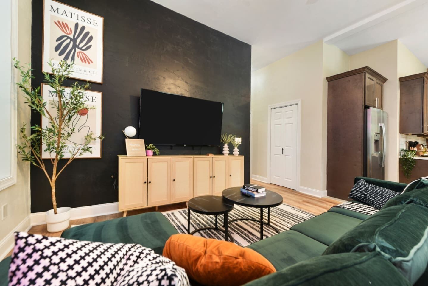 Un salon moderne avec un mur d’accent de couleur foncée, un téléviseur à écran plat, un meuble en bois, un canapé vert et une petite table ronde.