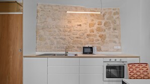 A kitchen with a stone wall, a microwave, an oven, and a sink. - Nid d'Ivresse, 1BR/1BA, 2 people (Paris)