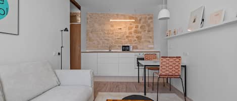Un espacio moderno para vivir con sofá, comedor con sillas, cocina con salpicadero de piedra y techo blanco.