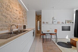 A modern kitchen with white cabinetry, a stone accent wall, and a dining area with a table and chairs. - Nid d'Ivresse, 1BR/1BA, 2 people (Paris)