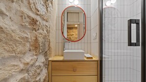 A bathroom with a stone wall, a wooden vanity with a mirror, and a tiled shower area. - Nid d'Ivresse, 1BR/1BA, 2 people (Paris)