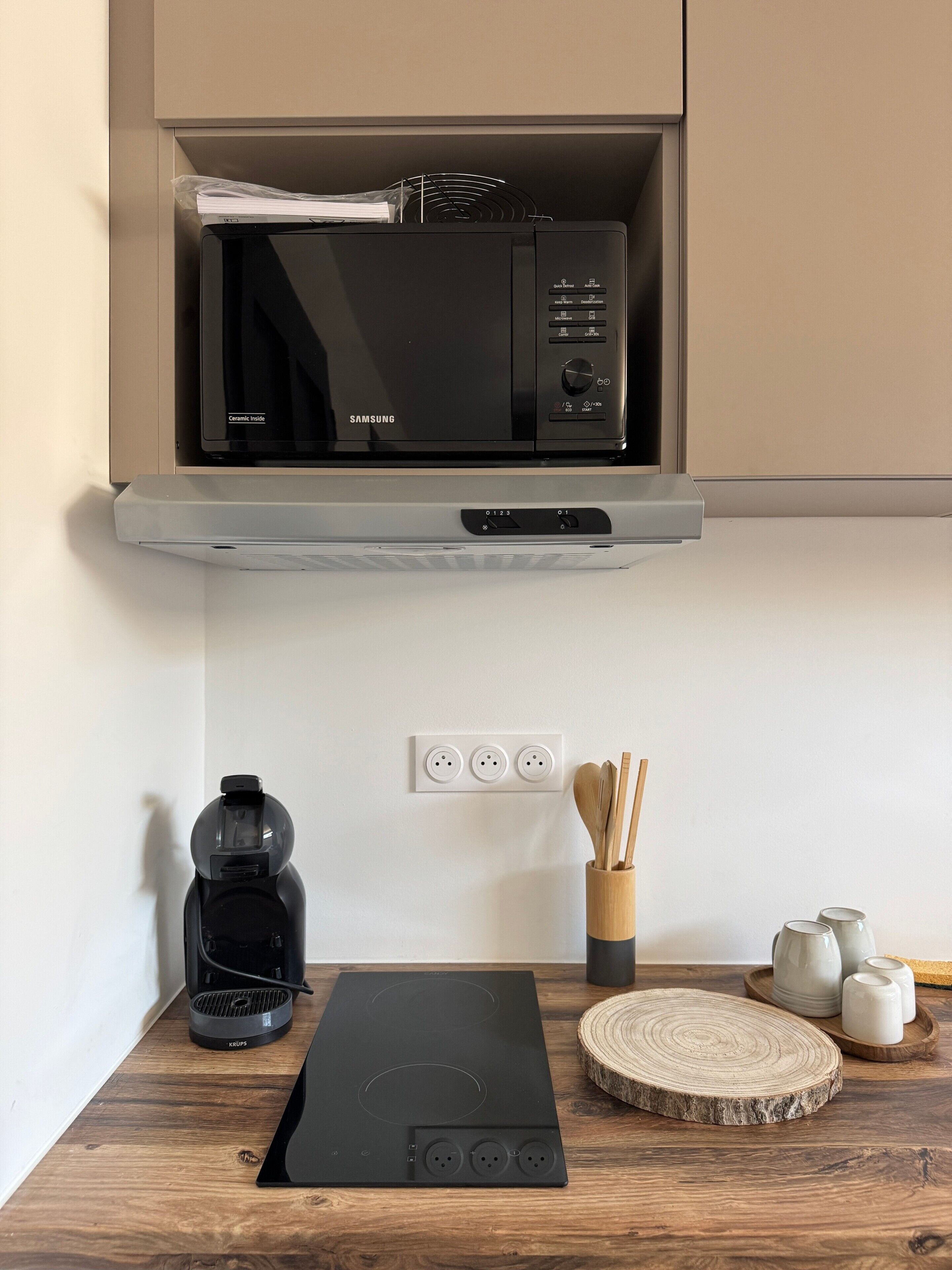 Une cuisine équipée d’un four à micro-ondes, d’une machine à café et d’une plaque de cuisson à induction moderne.