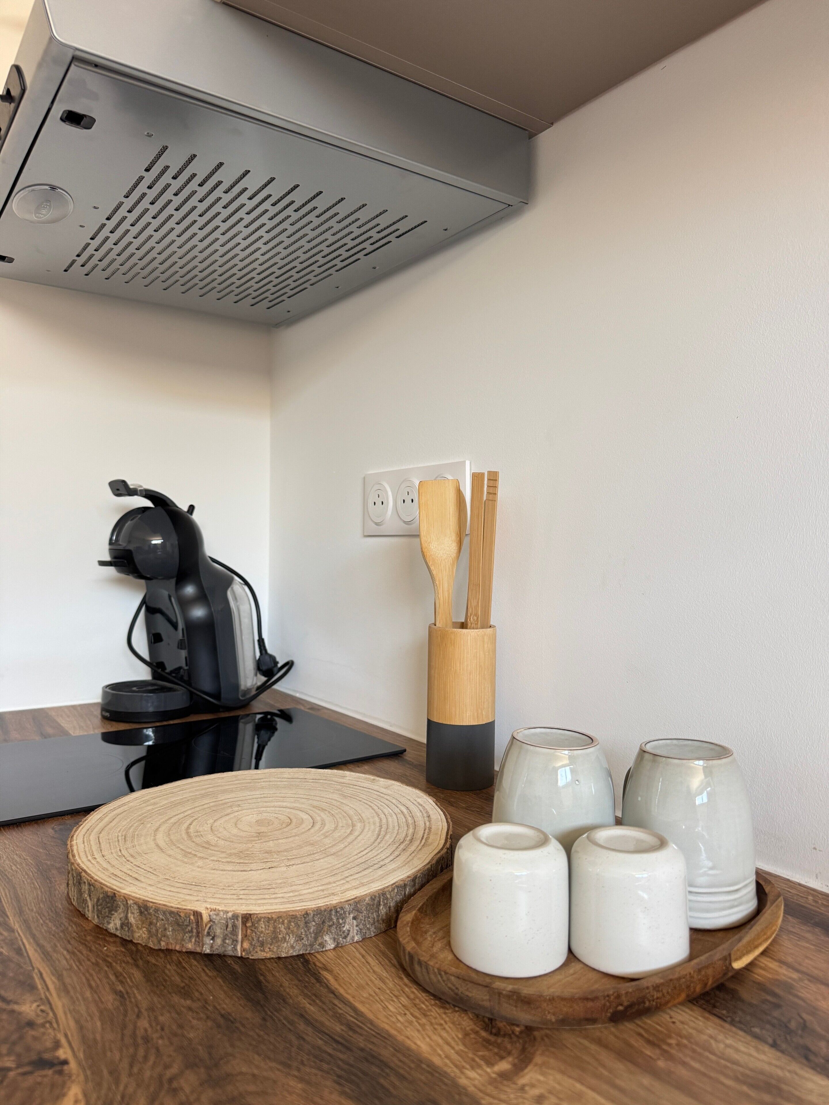 Angolo cottura con macchina da caffè, utensili in legno e tazze di ceramica su un vassoio di legno.