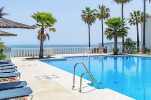 Ein Schwimmbecken mit freiem Blick auf das Meer, umgeben von Palmen und Liegestühlen.