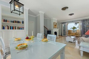 Un coin repas avec une table en verre, des chaises blanches et une bibliothèque remplie de livres.