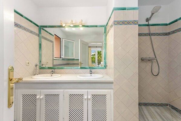 Une salle de bain avec deux lavabos, une douche et un miroir avec éclairage intégré.
