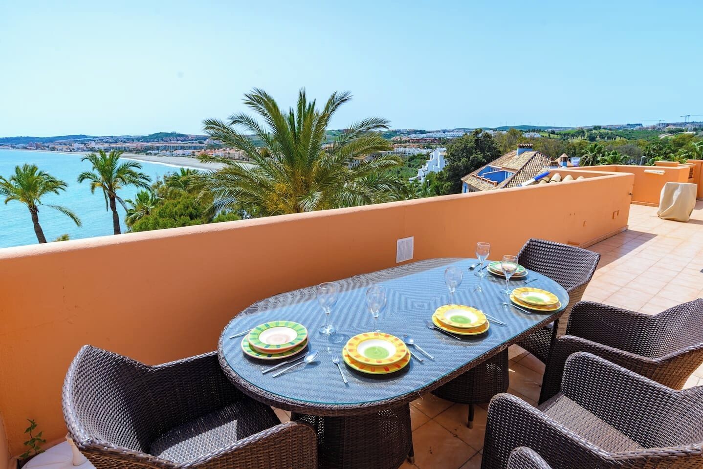 Un espace de restauration en plein air avec une table dressée pour quatre personnes, offrant une vue sur un paysage côtier.