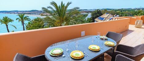 Un área de comedor al aire libre con una mesa dispuesta para cuatro personas, con vista a un paisaje costero.