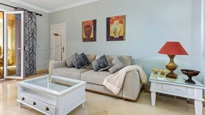 Een woonkamer met een bank, een glazen salontafel, een bijzettafeltje met een lamp en kunst aan de muur.