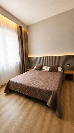 A modern hotel room with a large bed, wooden flooring, and a headboard with vertical lines.