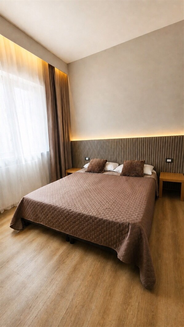 A modern hotel room with a large bed, wooden flooring, and a headboard with vertical lines.