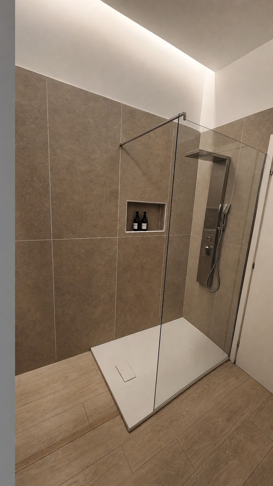 Eine moderne Dusche mit Glastür, einem integrierten Ablagebereich für Pflegeprodukte und Holzboden.