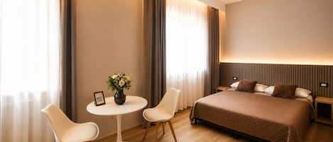 Una habitación de hotel con una cama, dos sillas, una mesita y un jarrón de flores.