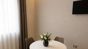 A modern dining area with a round table, four chairs, a vase with flowers, and a flat-screen TV mounted on the wall.