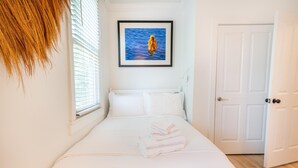 Ein Schlafzimmer mit einem Bett, einem gerahmten Bild an der Wand, einer Tür und einem Fenster mit Jalousien.