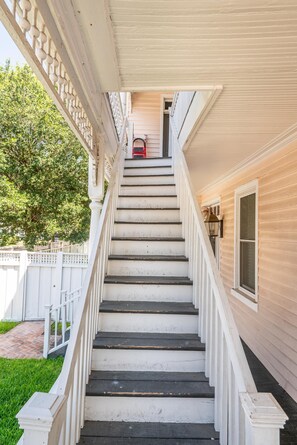 A staircase leading to a second-floor entrance of a building with a white exterior and a covered porch area. - Walk to King St | Spacious Charleston Stay (Charleston)