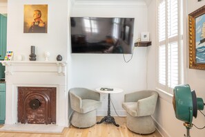 A living room with a fireplace, a television mounted on the wall, two armchairs, and a small table. - Walk to King St | Spacious Charleston Stay (Charleston)