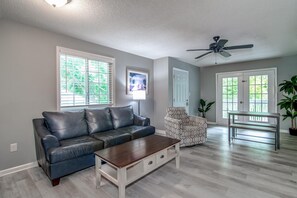 A living room with a leather sofa, a coffee table, a patterned armchair, and a dining table. - Hammock Haven | Walk to Marshwalk! (Murrells Inlet)