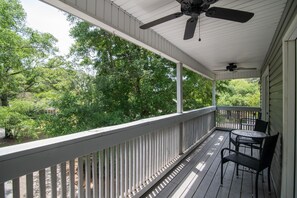 A covered porch with a ceiling fan, a table with chairs, and a view of a wooded area. - Hammock Haven | Walk to Marshwalk! (Murrells Inlet)