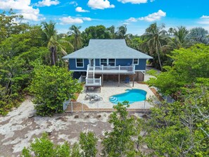 A two-story house with a pool, surrounded by lush greenery and palm trees. - Mollymawk Cottage: Peaceful Pool Home Near Beaches, Golf & Island Adventures (Sanibel)