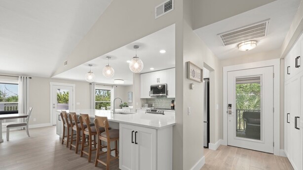 A modern kitchen with a central island, bar stools, and a dining area with a view. - Mollymawk Cottage: Peaceful Pool Home Near Beaches, Golf & Island Adventures (Sanibel)