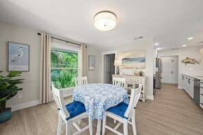 A modern kitchen with white cabinets, a refrigerator, and a dining area with a table and chairs. - Mollymawk Cottage: Peaceful Pool Home Near Beaches, Golf & Island Adventures (Sanibel)