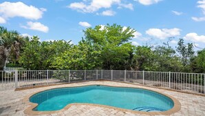 A swimming pool with a white fence, surrounded by a brick patio and lush greenery. - Mollymawk Cottage: Peaceful Pool Home Near Beaches, Golf & Island Adventures (Sanibel)