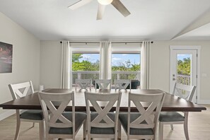 A dining area with a table and chairs, a ceiling fan, and a view through large windows. - Mollymawk Cottage: Peaceful Pool Home Near Beaches, Golf & Island Adventures (Sanibel)