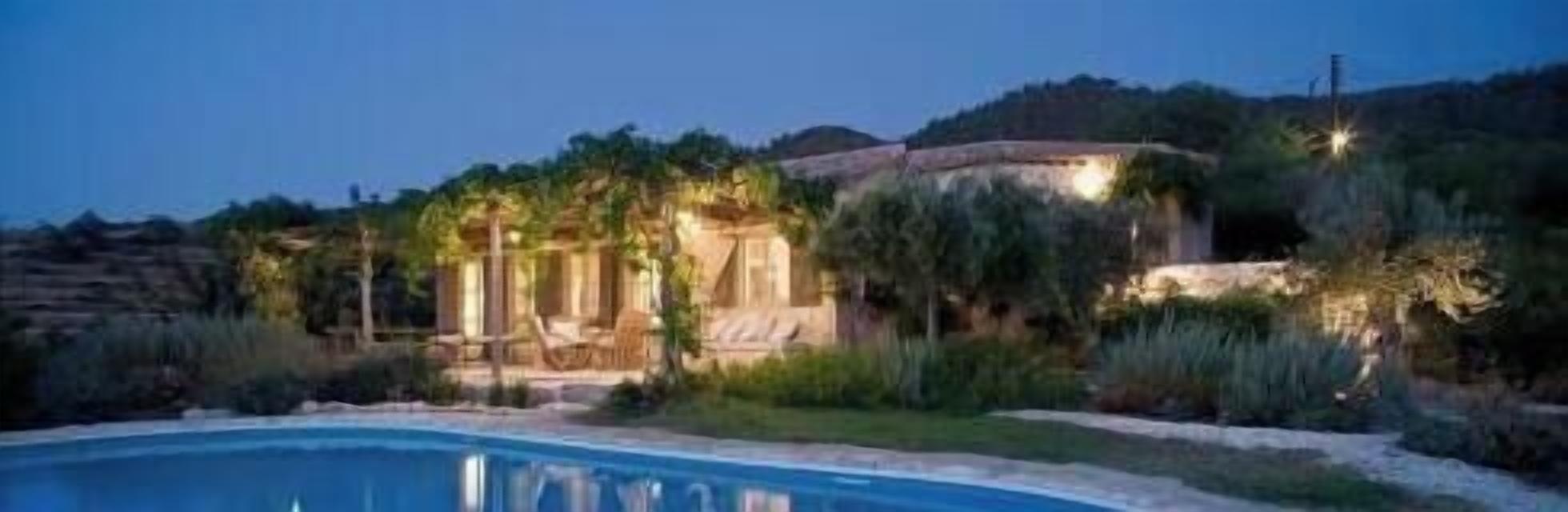 A poolside view of a villa with a swimming pool, surrounded by lush greenery and a hillside backdrop.