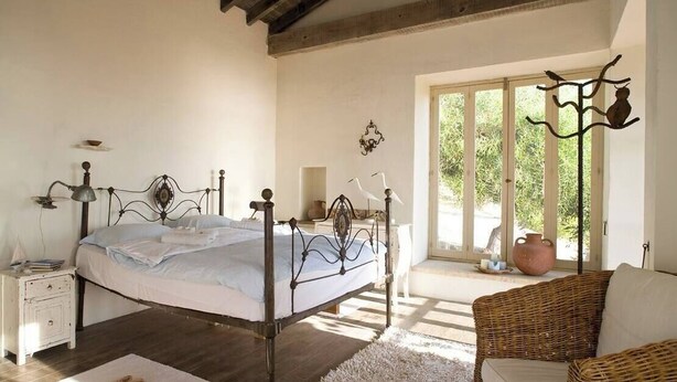 A bedroom with a bed, bedside table, lamp, and a wicker chair. - Aphrodite's Oasis with Private Pool (Pomos)