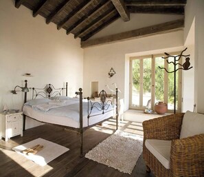 A bedroom with a bed, bedside table, lamp, and a wicker chair. - Aphrodite's Oasis with Private Pool (Pomos)