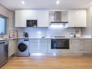 Une cuisine moderne équipée d’appareils électroménagers en acier inoxydable, d’un four encastré et d’un lave-linge.