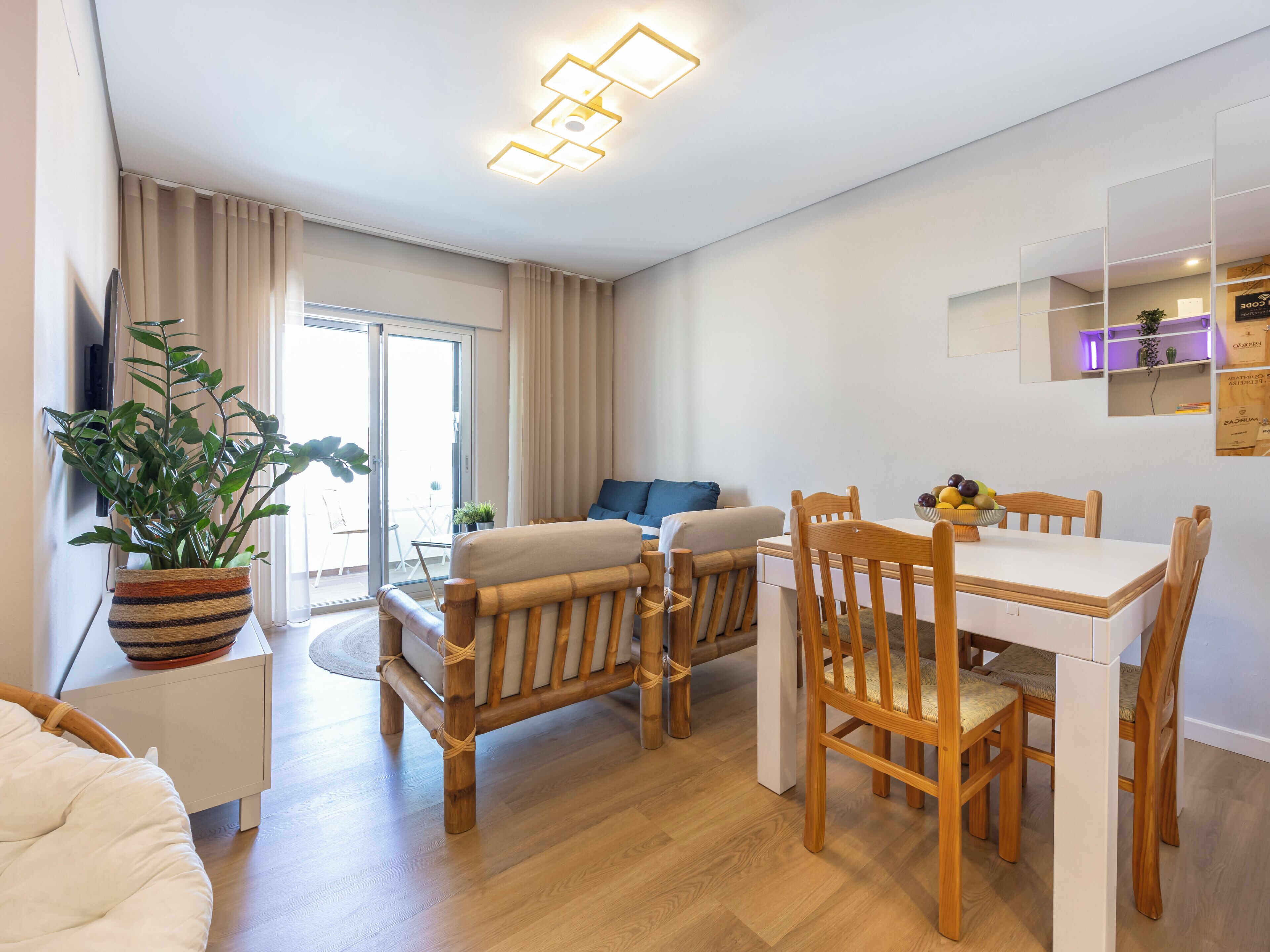 En moderne stue med en sofa, et spisebord med stole, en potteplante og en skydedør, der fører til et udendørs område.