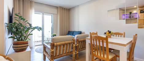 Una sala de estar moderna con un sofá, una mesa de comedor con sillas, una planta en maceta y un ventanal corredero que da a un espacio exterior.