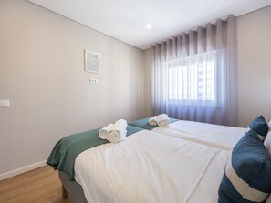 A hotel room with two beds, a window with curtains, a wall-mounted light switch, and a framed picture. - Algarve Sun Apartment - Family Home in Portimão (Portimão)