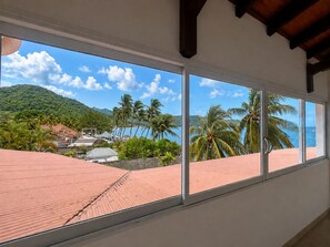 A room with large windows offering a view of a beach, palm trees, and a mountain. - Dream Villa in Martinique, with a Pool and Direct Access to the Beach (Les Anses-d'Arlet)