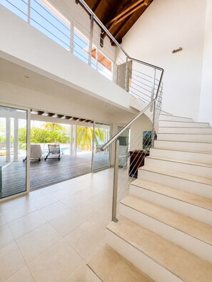 A modern interior with a staircase leading to an upper level, a glass door leading to an outdoor area, and a view of the outdoors. - Dream Villa in Martinique, with a Pool and Direct Access to the Beach (Les Anses-d'Arlet)