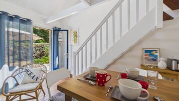 A dining area with a wooden table set for two, a wicker chair, and a staircase leading to an upper level.