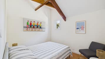 A bedroom with a bed, a chair, and two wall-mounted pictures.