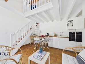 A modern kitchen with white cabinets, a dining area with wicker chairs, and a staircase leading to an upper level.