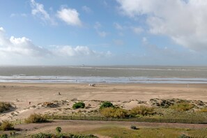 Une vaste plage de sable, avec une clôture au premier plan, un ciel dégagé et une vue lointaine sur la mer.