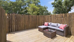 Un patio al aire libre con piso de madera, un sofá de mimbre con cojines y una mesita.