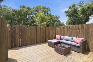 An outdoor patio with a wooden deck, a wicker sofa with cushions, and a small table. - NEW!  Muse on 10th - We Love Doggies! (Wilmington)