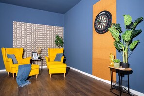 Ein Zimmer mit zwei gelben Sesseln, einer Dartscheibe, einer Wand mit Muster und einem Blumentopf.
