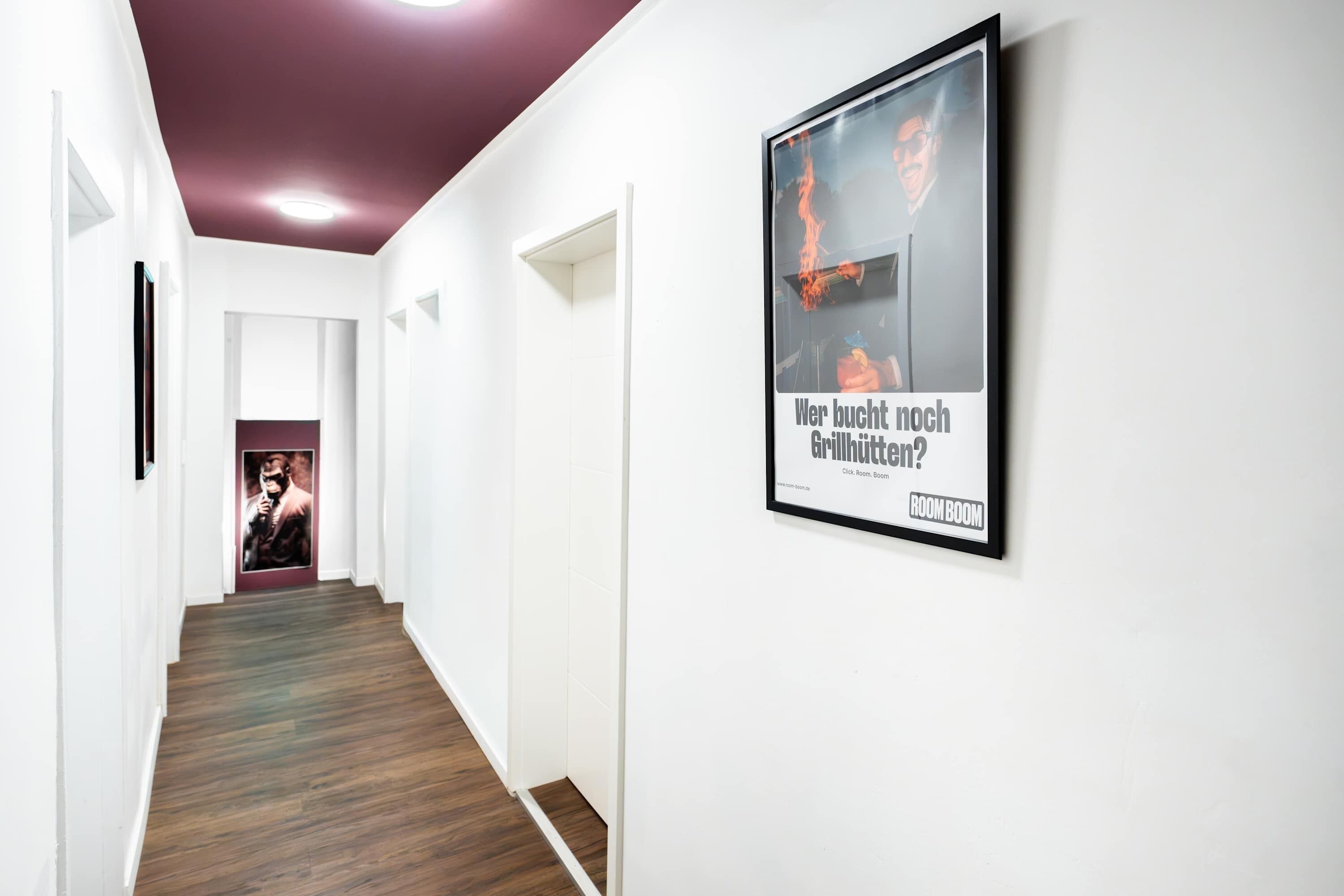 Un couloir avec un plancher en bois, des murs blancs et une affiche encadrée accrochée au mur.