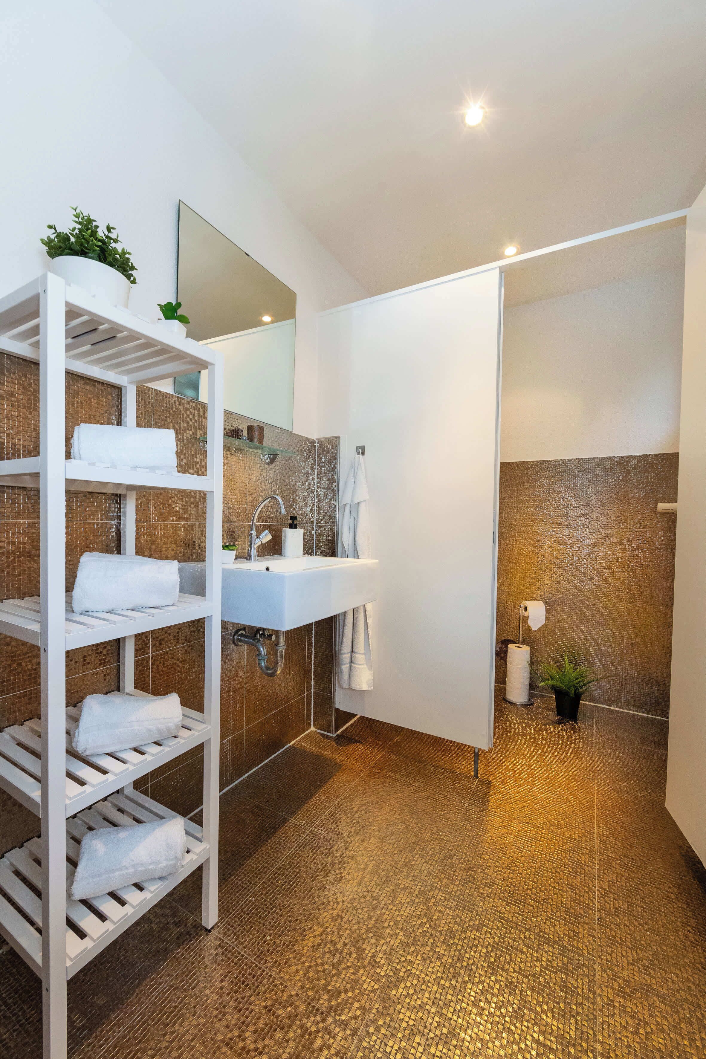 Ein modernes Badezimmer mit einem weißen Waschbecken, einem Spiegel und einem Ablagebereich mit Handtüchern.